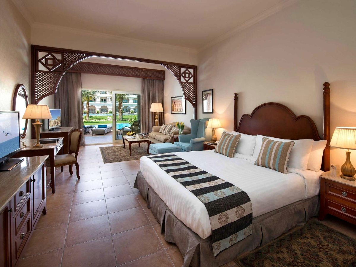 A ground-floor room with arched patio doors onto a terrace, a large bed, sofa seating and pool and garden views.