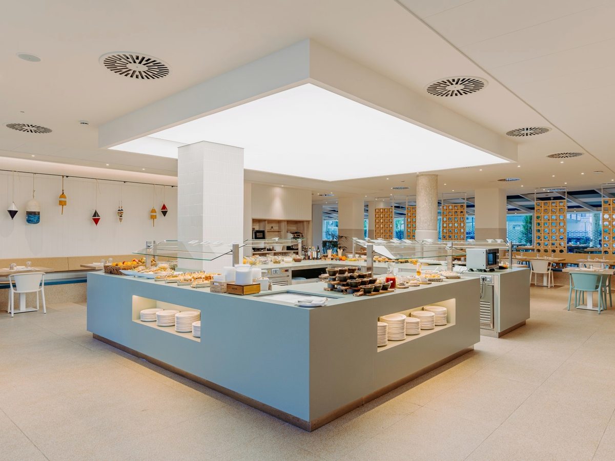A large L-shaped buffet counter with dishes and stacked plates around a central serving island in a bright dining room