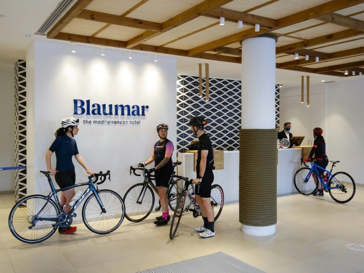 Cyclists with road bikes at the Blaumar reception desk, under a wood-beamed ceiling with a large Blaumar sign on the wall