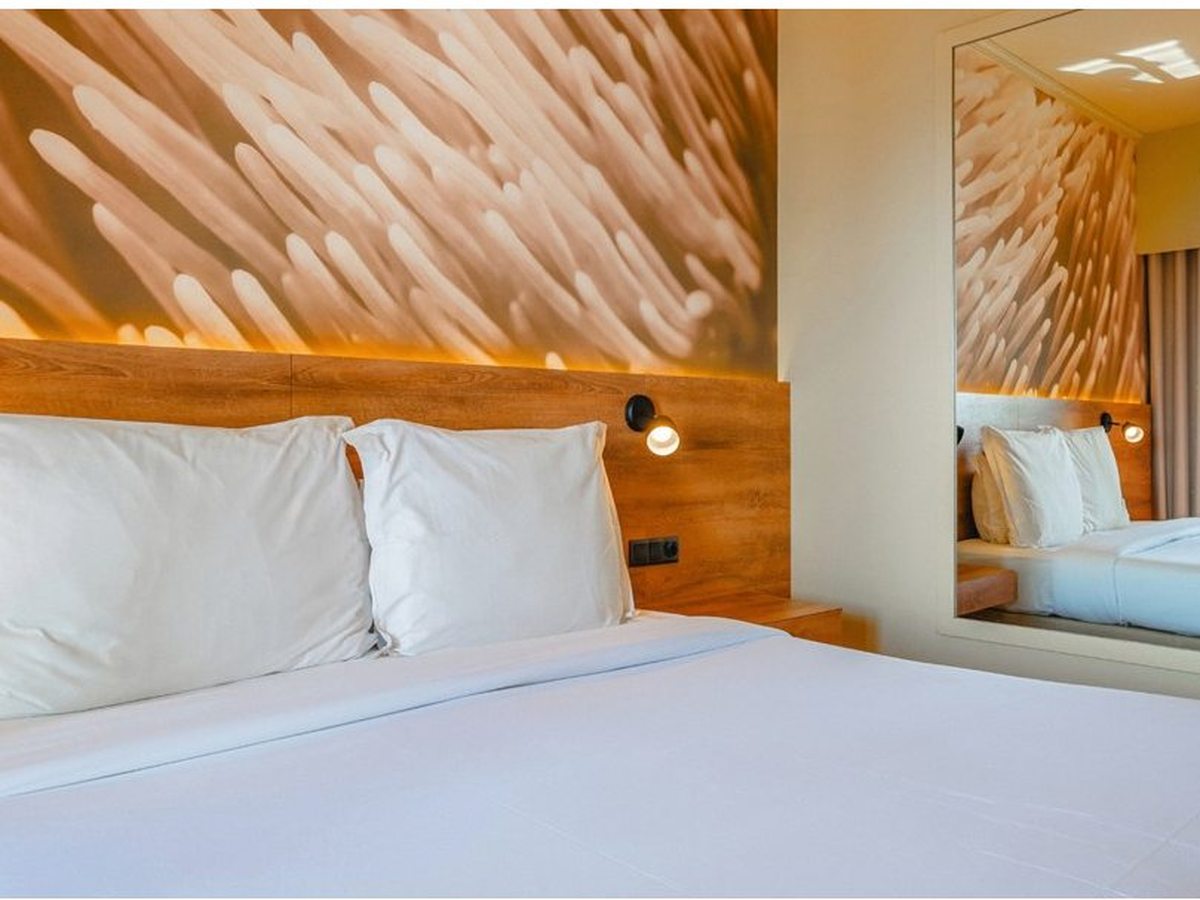 Double room with a white-linen double bed, a wooden headboard and a mirror on the facing wall.