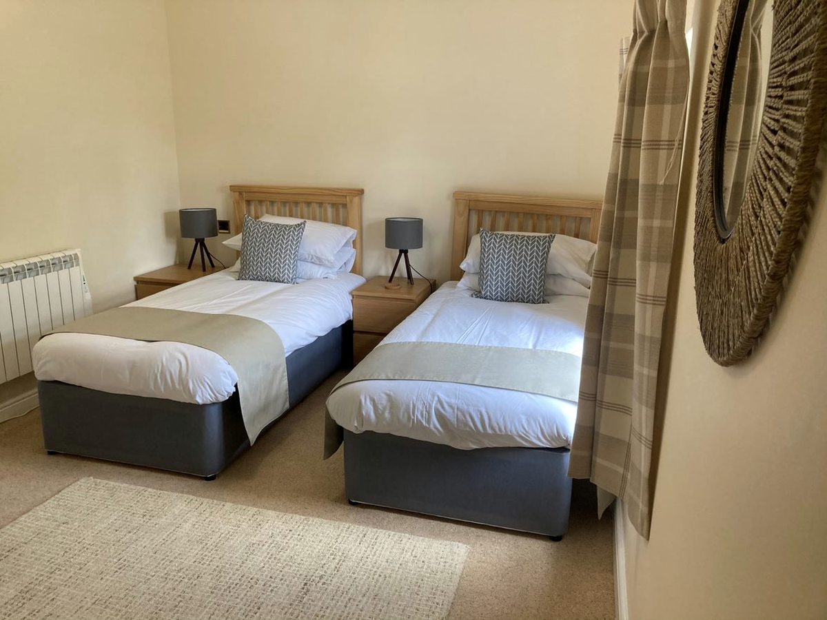 A twin bedroom with two single beds made up in white linen and a round mirror on the wall.