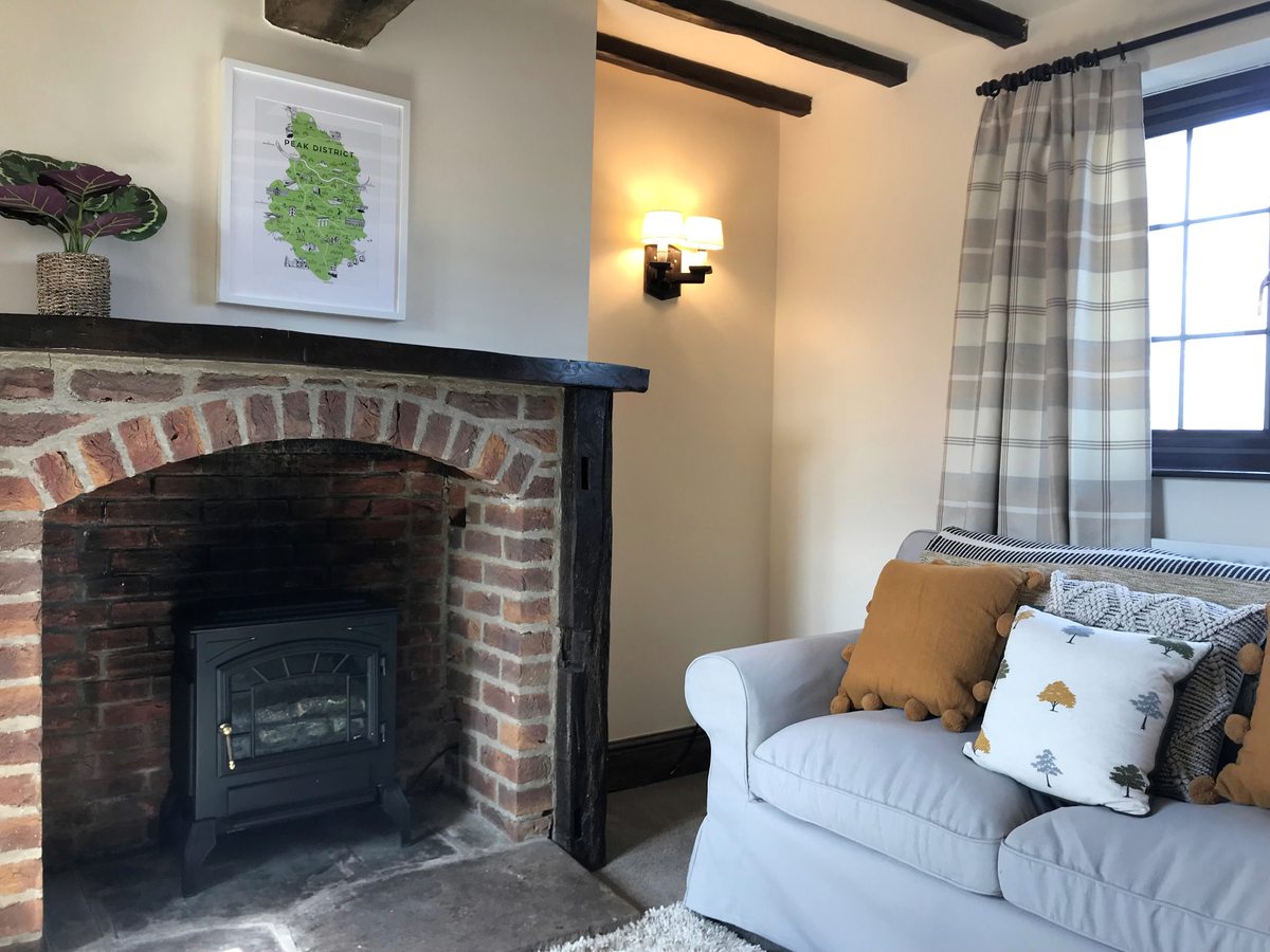 A cottage sitting room with exposed beams, a brick fireplace with a wood-burning stove and soft sofas.