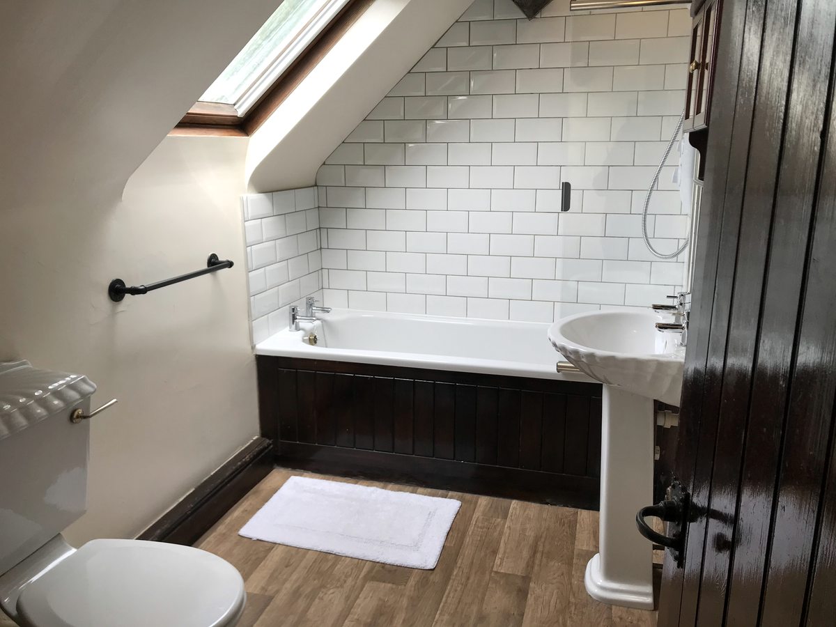 A family bathroom with a bath and shower over it, a basin and white metro tiles under a sloping ceiling.
