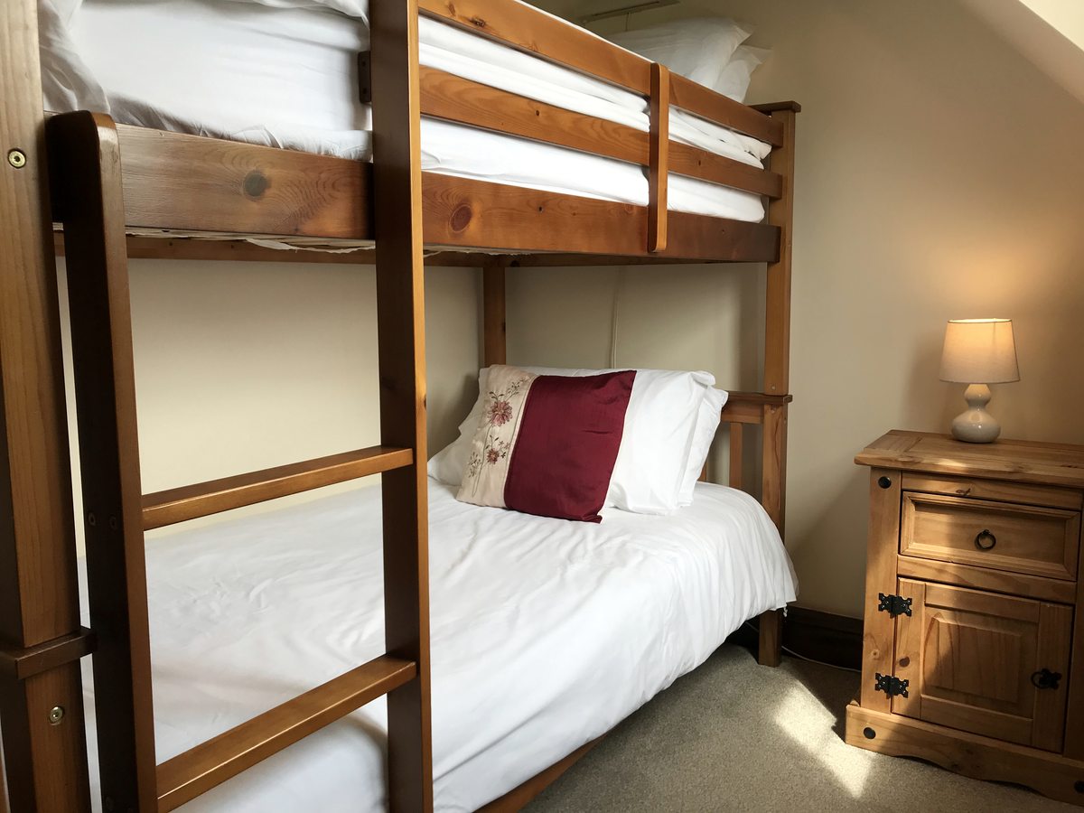 A wooden bunk bed made up with white and red linen beside a chest of drawers.
