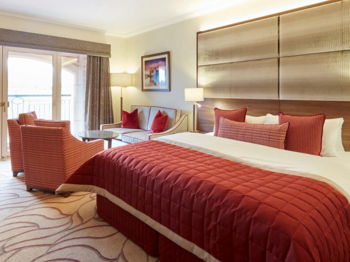 A Resort Hotel bedroom with a large bed under a red bedspread and a small seating area of armchairs around a glass coffee table.