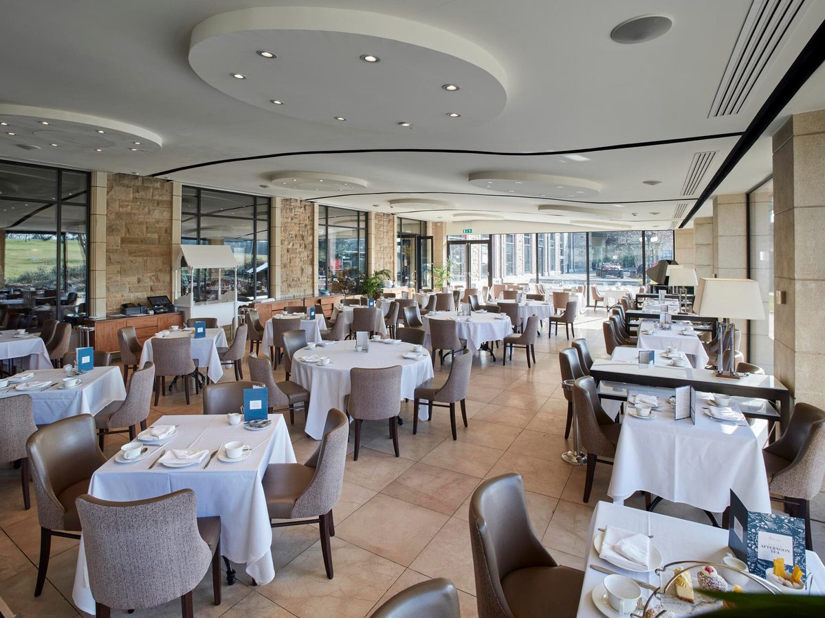 A spacious hotel restaurant with white-clothed tables, stone columns and a curved ceiling, lit by tall windows onto the garden.