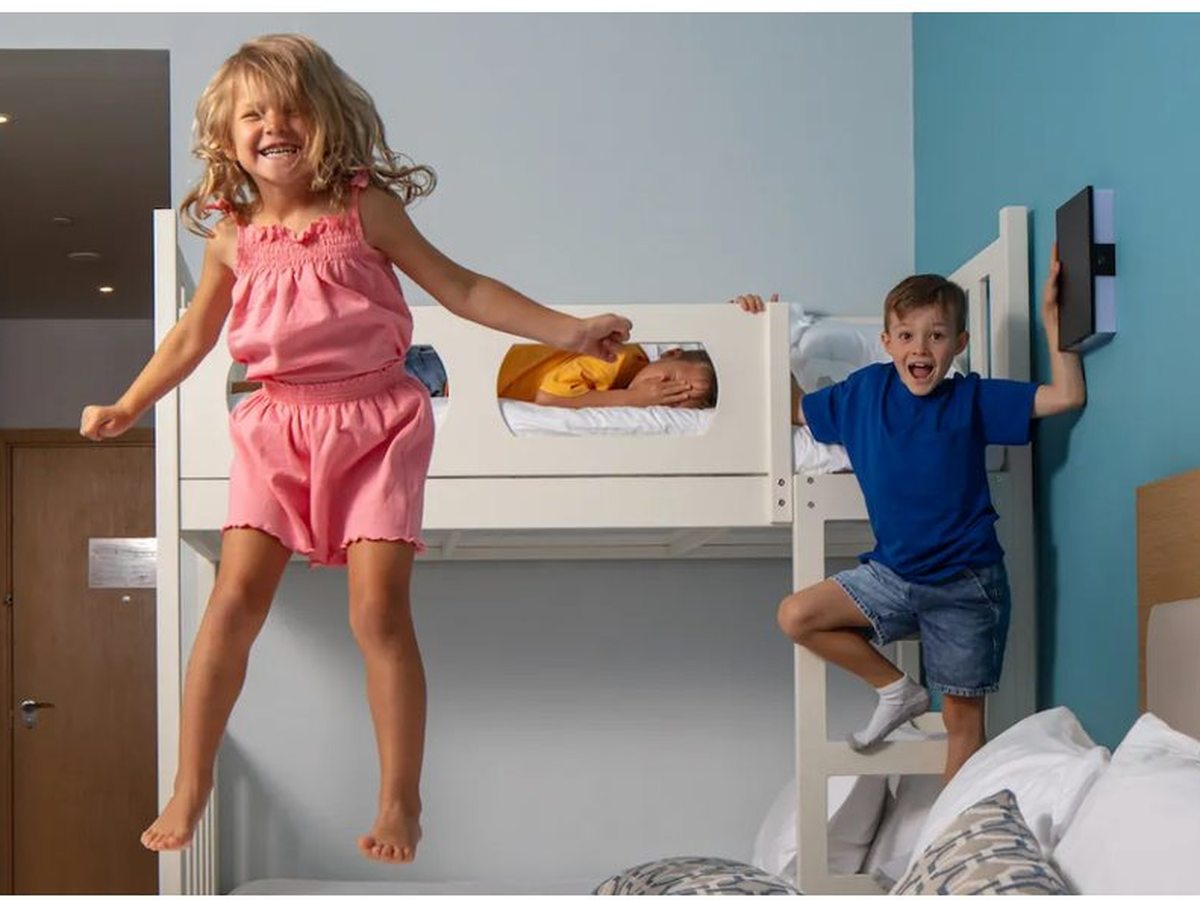 Two children playing on white bunk beds beside a double bed against a blue feature wall in a family room.