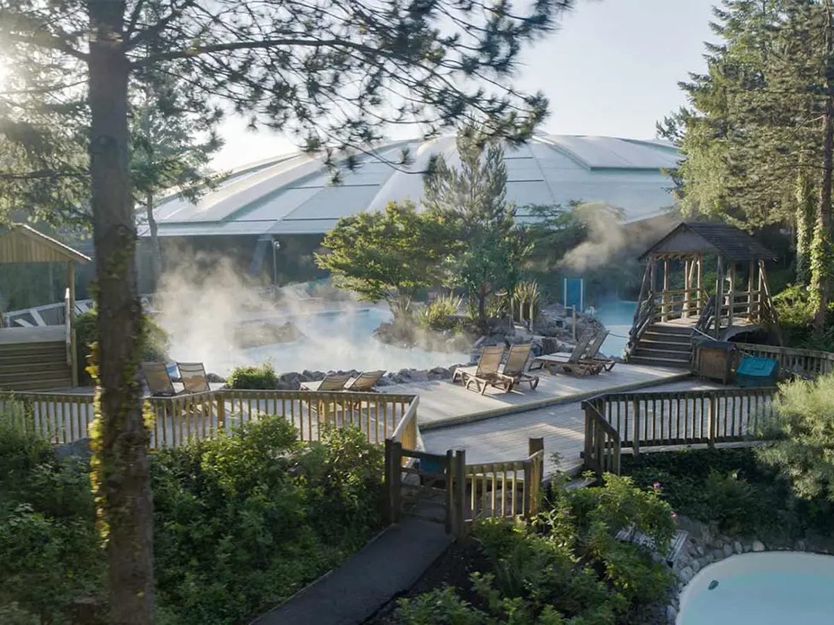 Steam rising off an outdoor pool on a timber deck with sun loungers, the glass dome of the pool building behind.