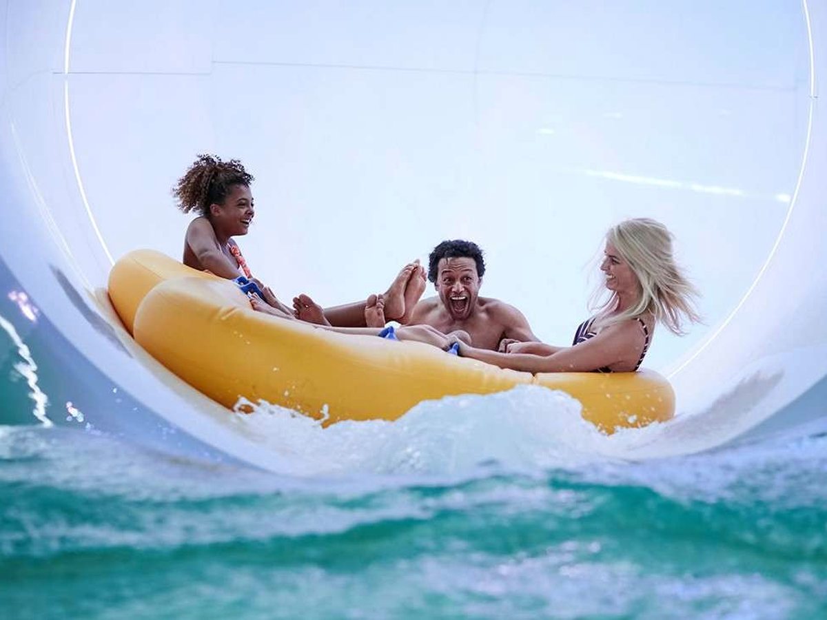 Three people riding a yellow inflatable raft down an enclosed water slide.