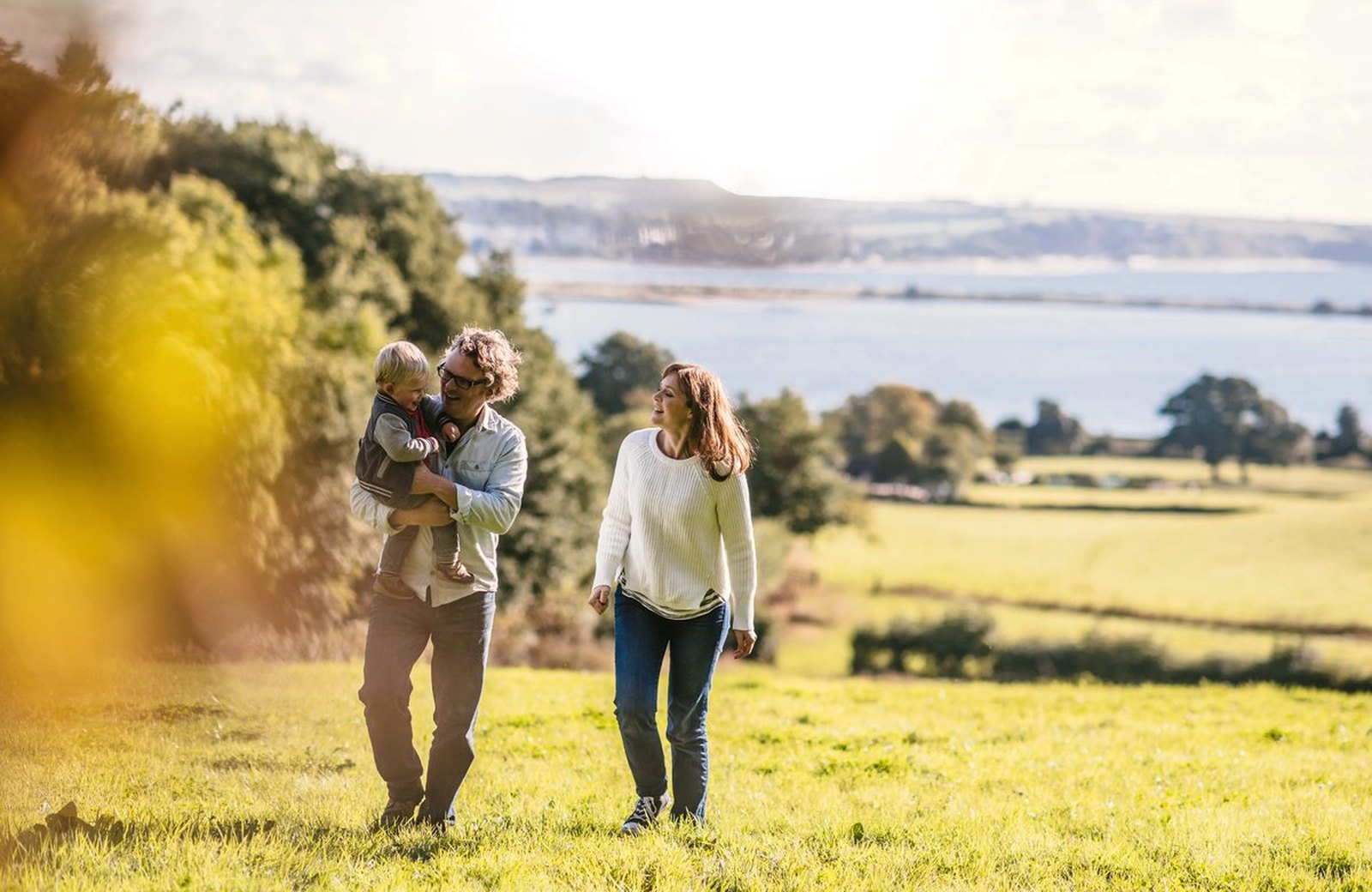 A family walking on a sunny grassy hillside above the Exe Estuary, with the South Devon coast in the distance.