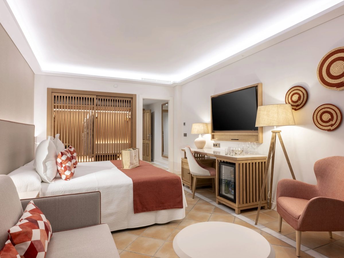 A room with a double bed, a pink armchair and a small sitting area with a round coffee table.