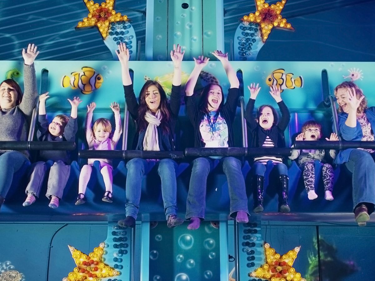 Families with their hands in the air on an undersea-themed indoor ride lit blue, with lit starfish on the walls