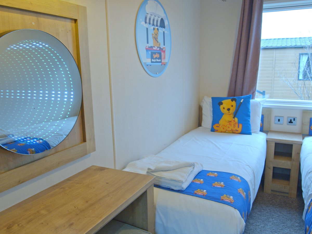 A child's single bed with Sooty-branded bedding and cushion, an infinity mirror on the wall and a Sooty Land picture