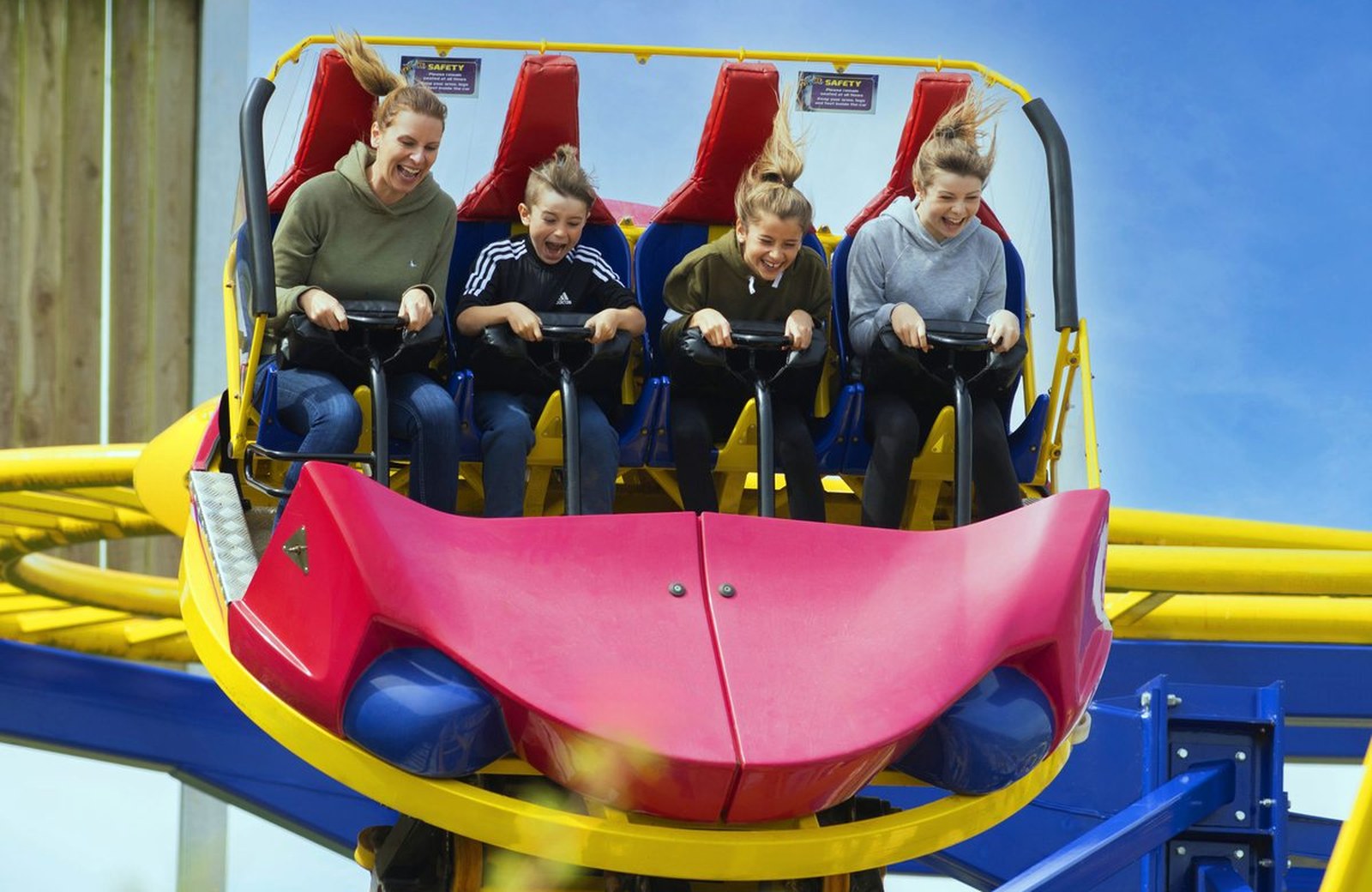 A family and children laughing on a bright yellow and red rollercoaster car against a blue sky at Crealy Theme Park in East Devon.