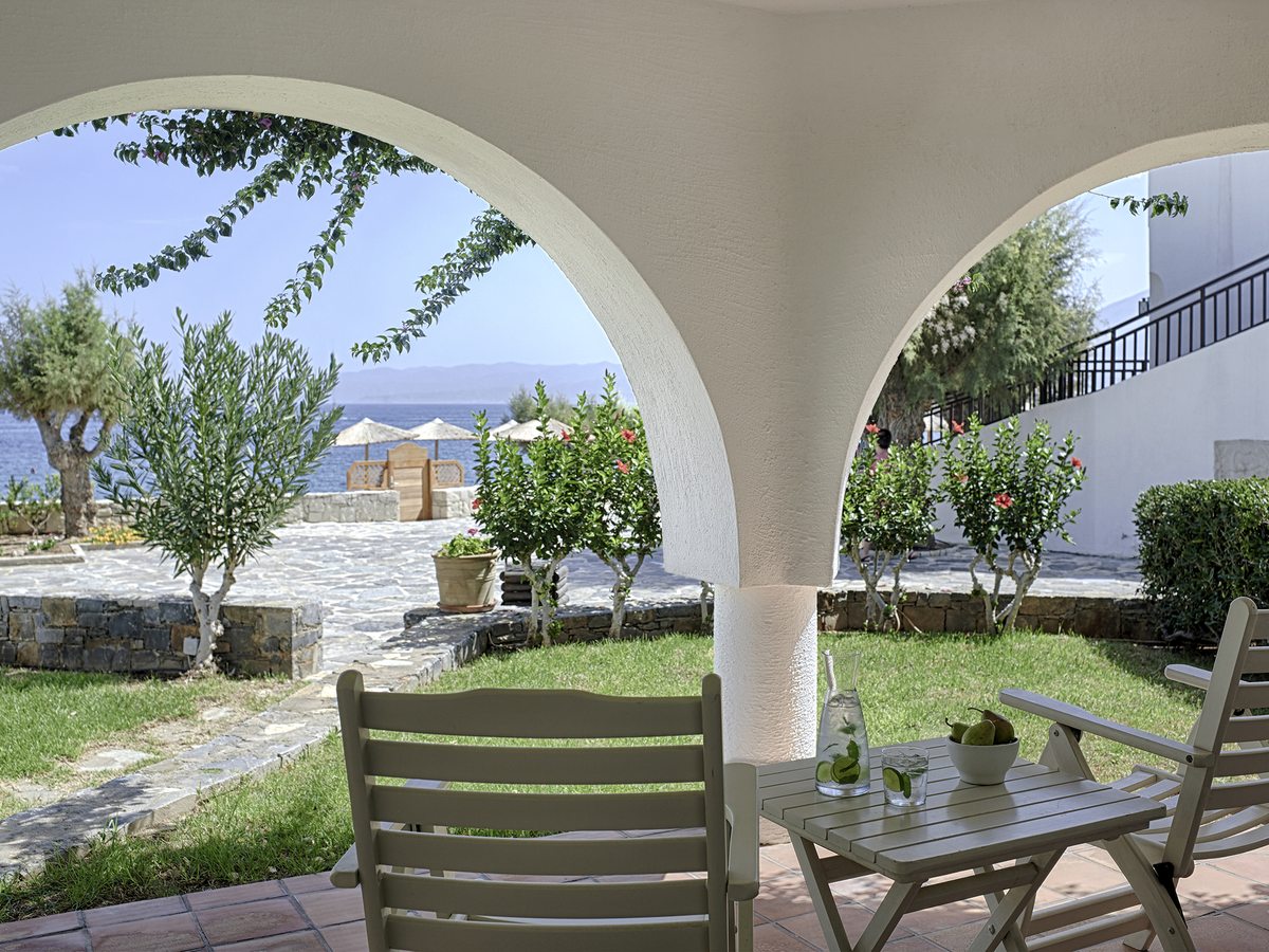 A stone-arched pergola terrace with garden chairs and tables looking out towards the sea