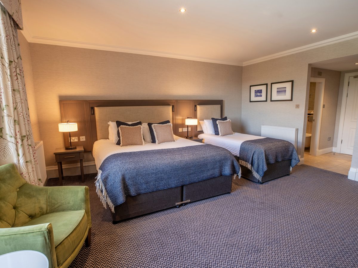 A family room with a double bed and a single bed side by side, a green armchair and an ensuite doorway.
