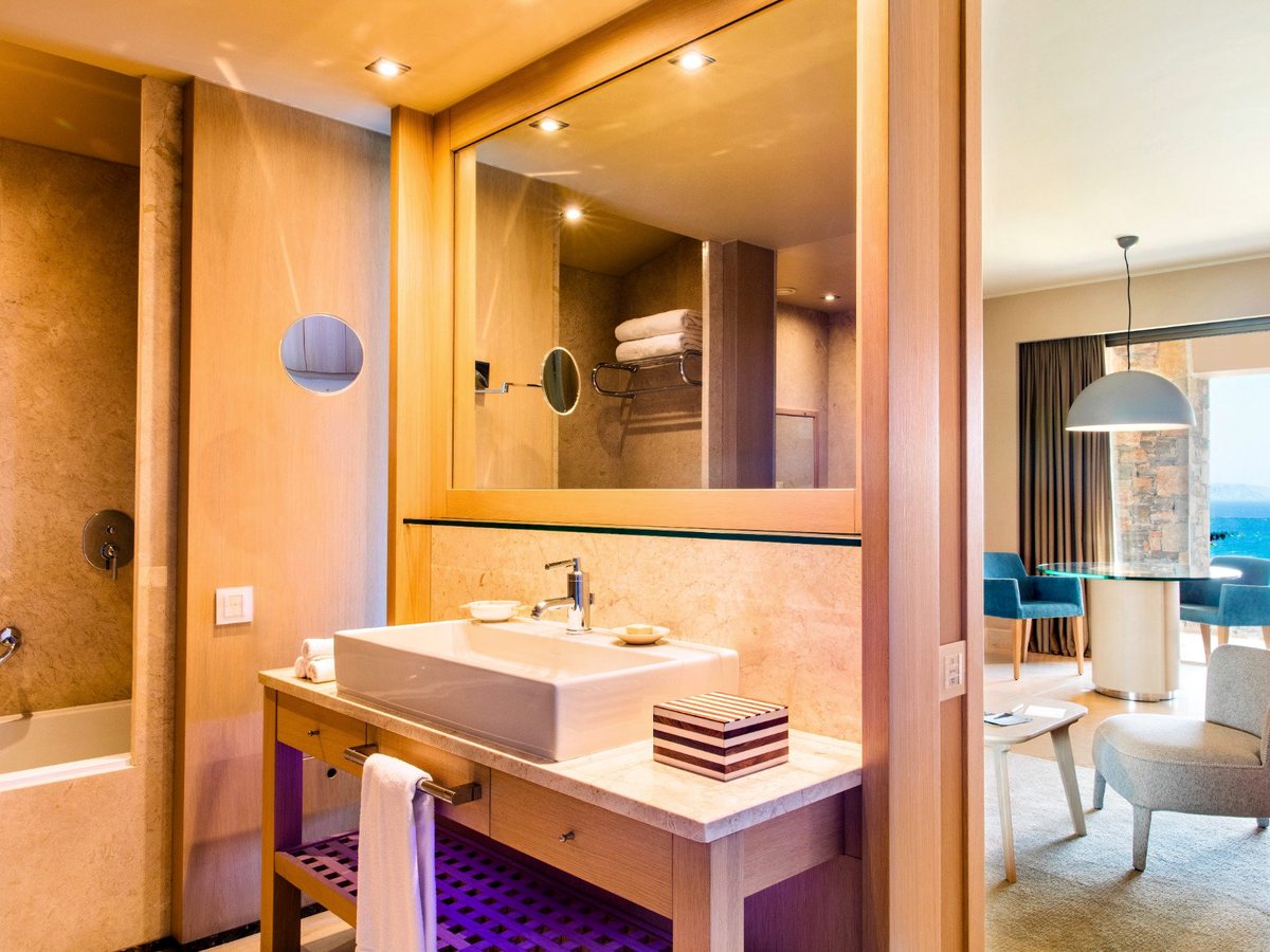 An open-plan bathroom with a recessed bathtub and a rectangular basin on a timber vanity, beside the suite's sitting area.