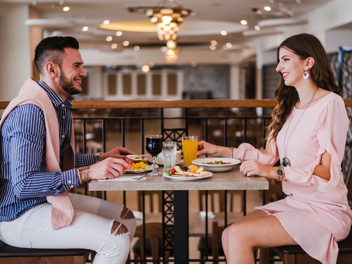 A couple at a table for two with plated meals and drinks in a restaurant with chandeliers.