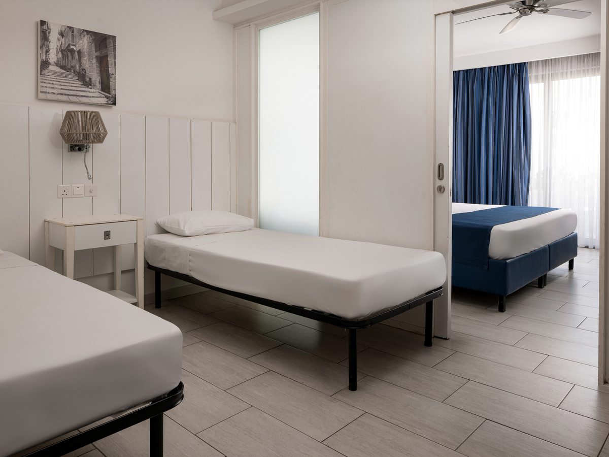 The second sleeping area of a family room with two single beds on raised bases and a sliding doorway through to an adjoining double bedroom.