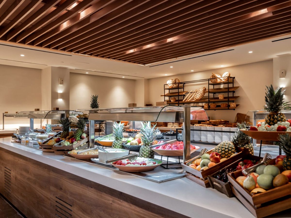 Fresh-fruit buffet counter with watermelon, pineapples and melons on raised wooden displays at a self-service station.
