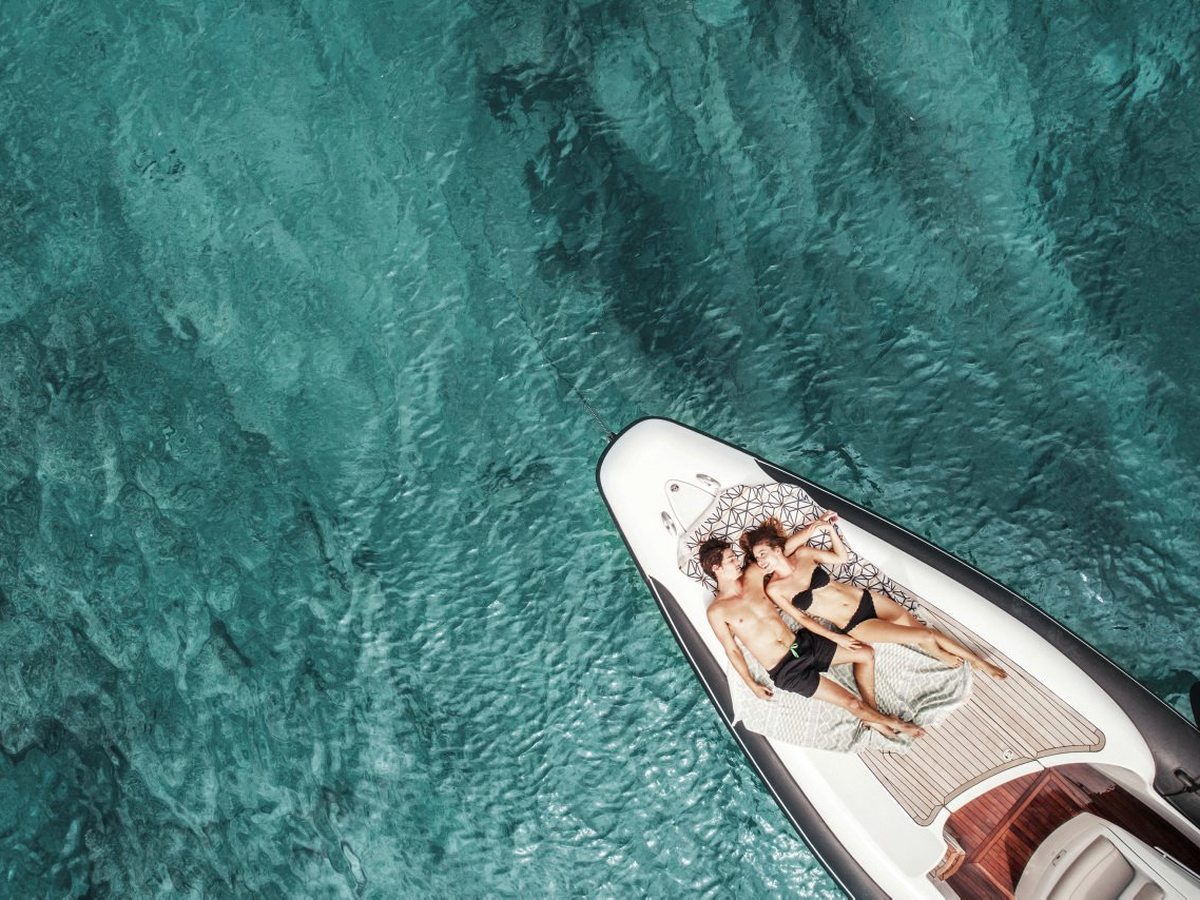 An aerial view of a small motorboat on clear turquoise water, two people aboard.
