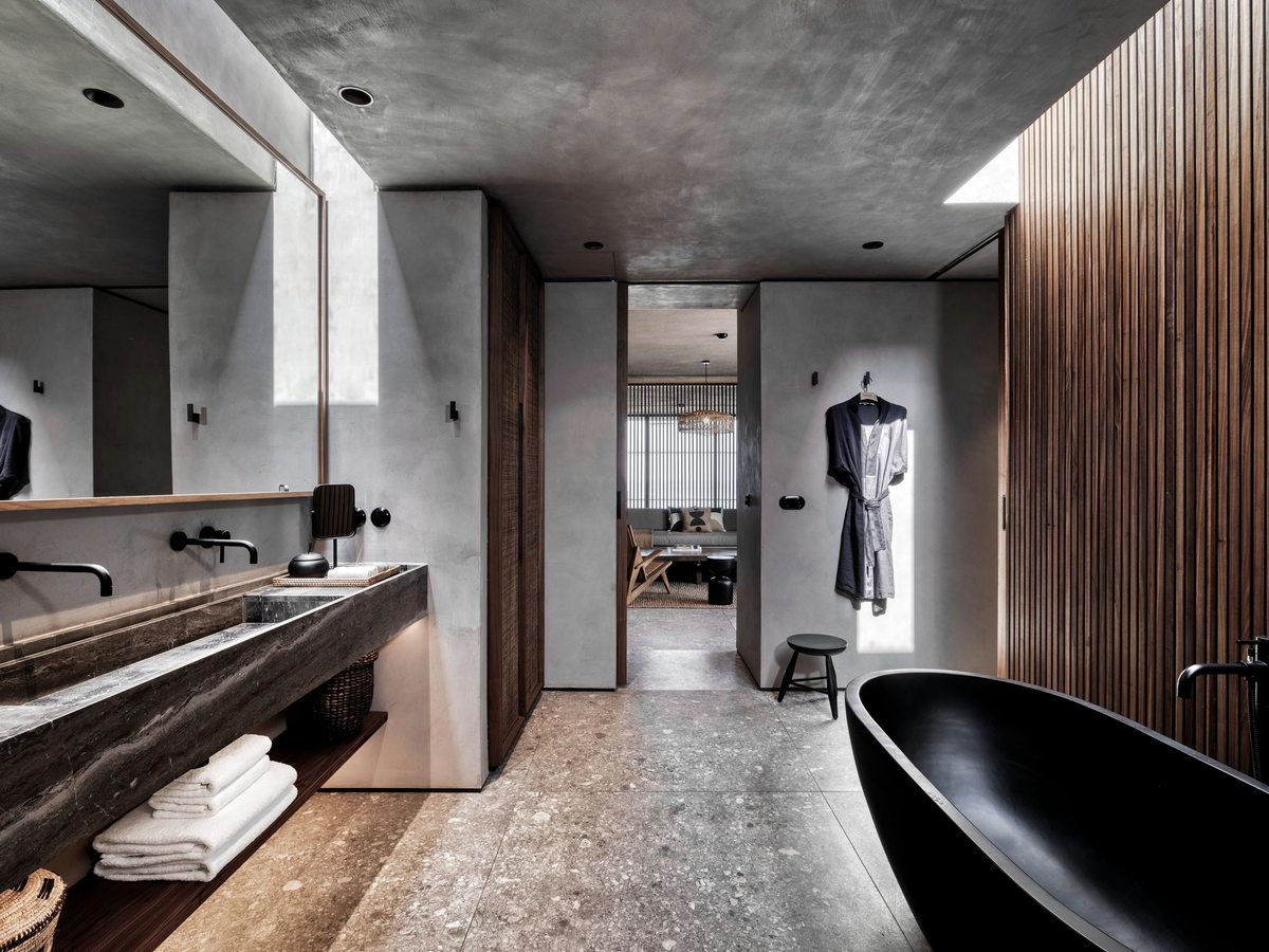 A bathroom with a freestanding black tub and a long stone vanity under warm lighting.