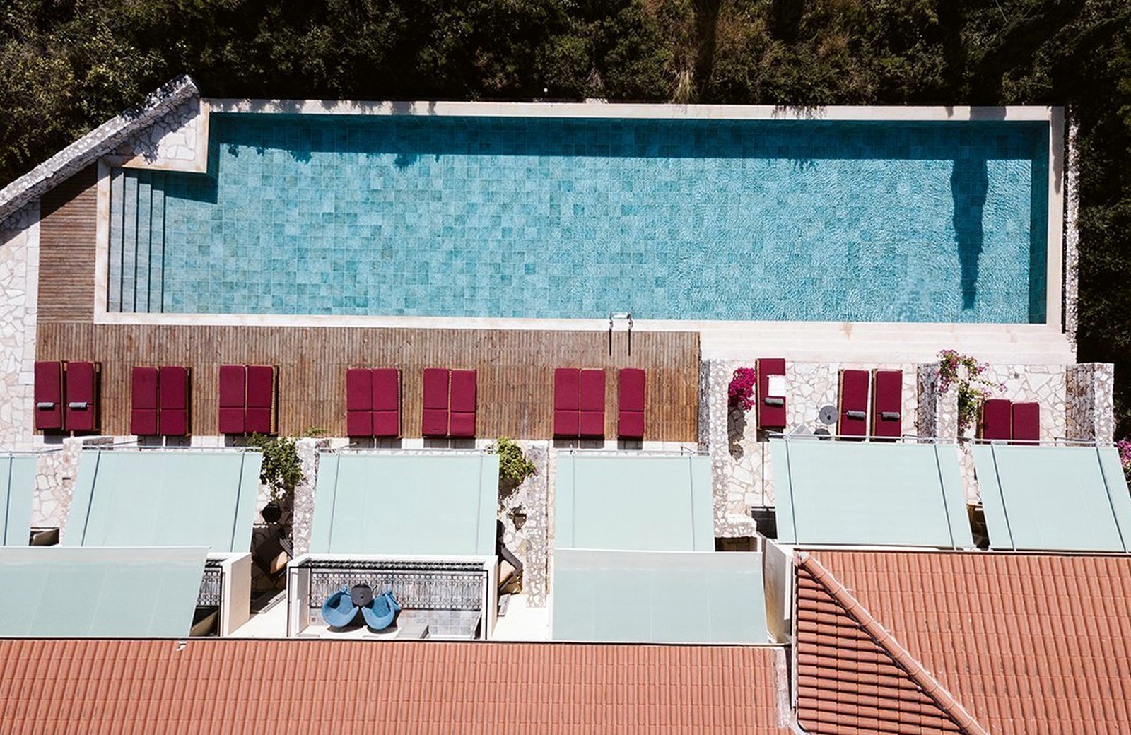An aerial view of the resort's pool, a row of red sunloungers along its timber deck and guest rooms terraced on the wooded hillside below.