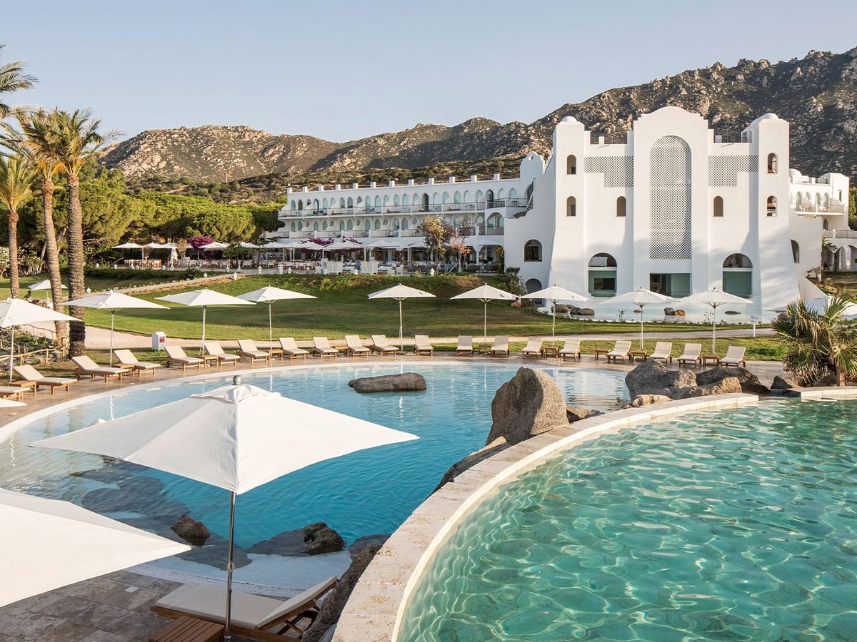 A two-level pool with large granite boulders and a parasol, the white latticework tower of the main building rising behind lawns.