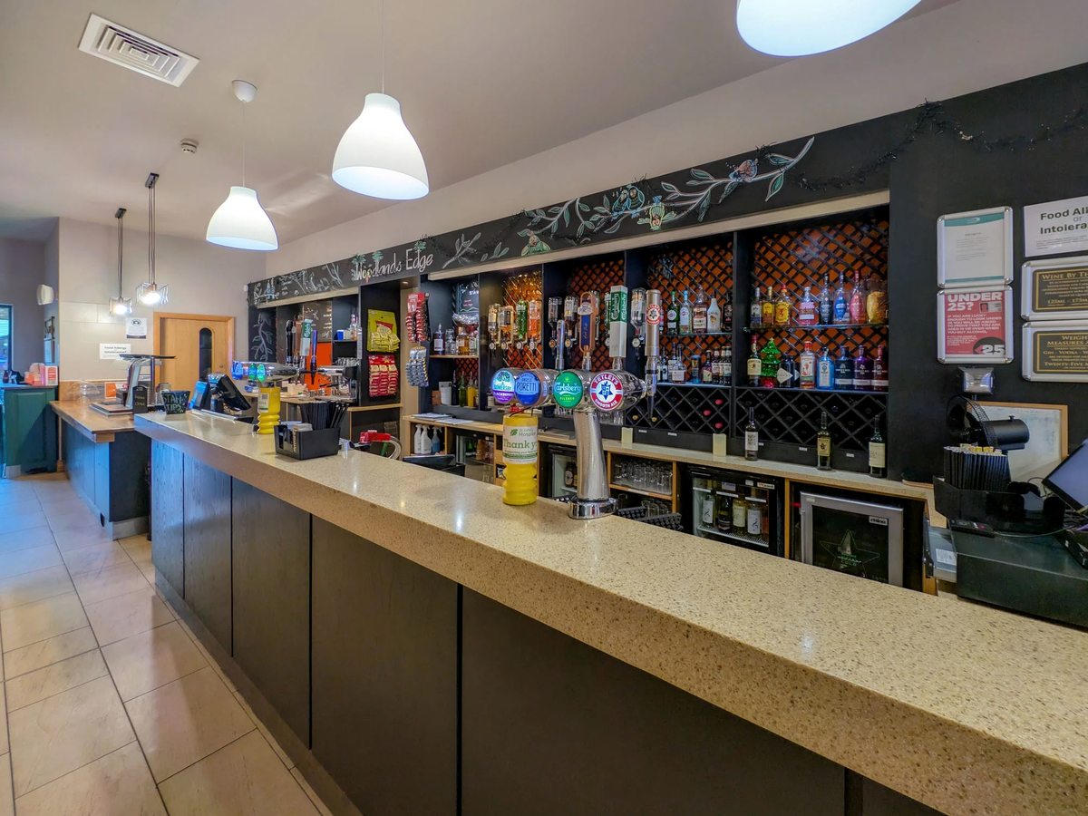 The Woodland Edge bar counter with beer taps, bottled drinks and a chalkboard behind.