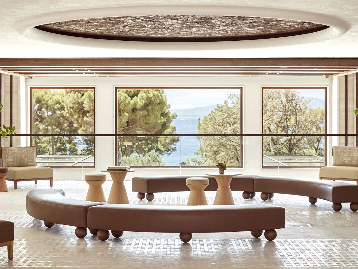 A curved cream sofa and cane armchairs in the lobby lounge, with floor-to-ceiling windows framing pine trees and the bay beyond.