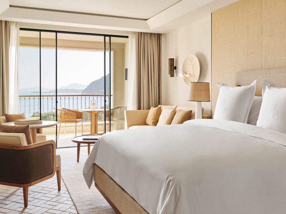 A king room with full-height glass doors folding back onto a terrace, looking out to the sea and mountains.