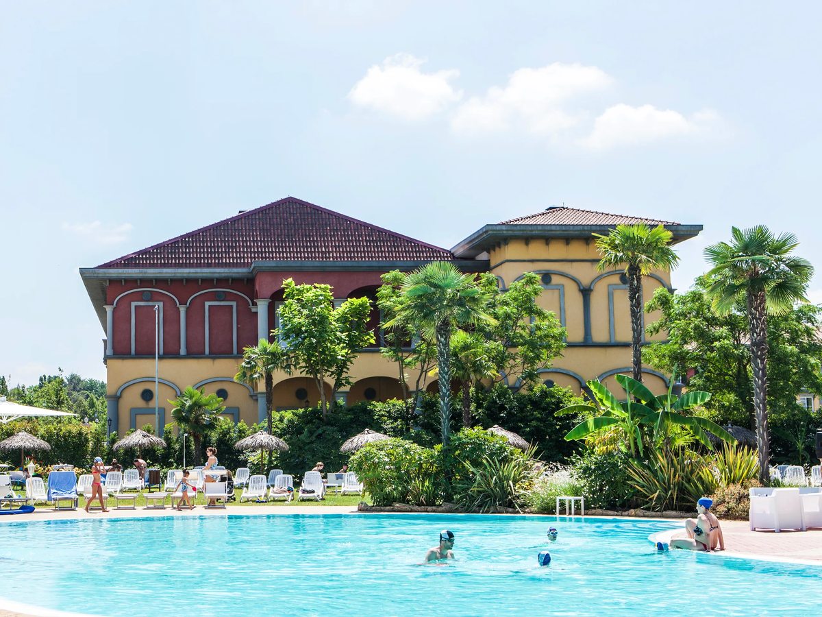 Guests swimming in the Blue Lagoon pool, with palms, planting and a resort building behind.