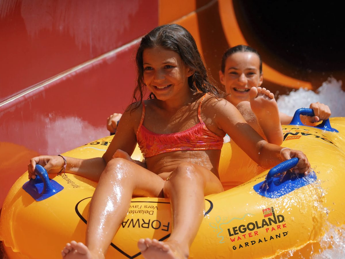 Two children on a yellow raft coming down an orange enclosed water slide at the LEGOLAND Water Park.