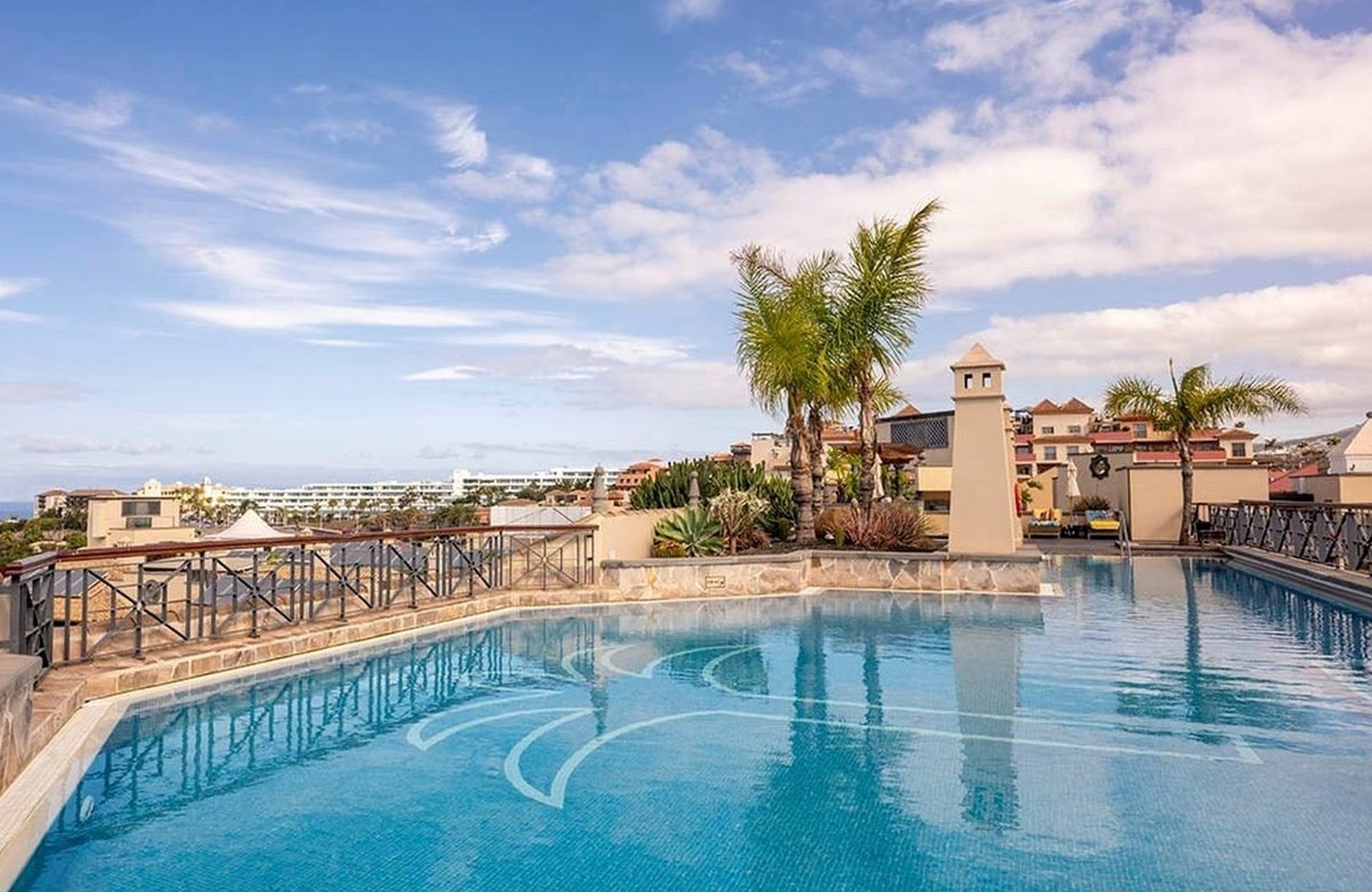 One of GF Isabel's pools, curving between the low-rise Canarian-village buildings and palms, with the sea beyond, in Costa Adeje, Tenerife.