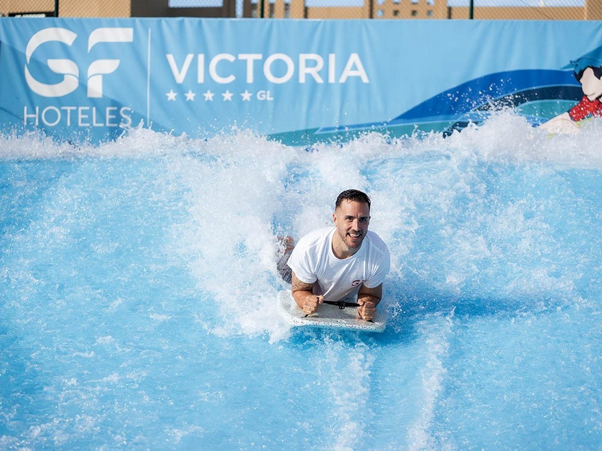 A man riding a bodyboard on a sheet of churning white water against a GF Victoria banner.