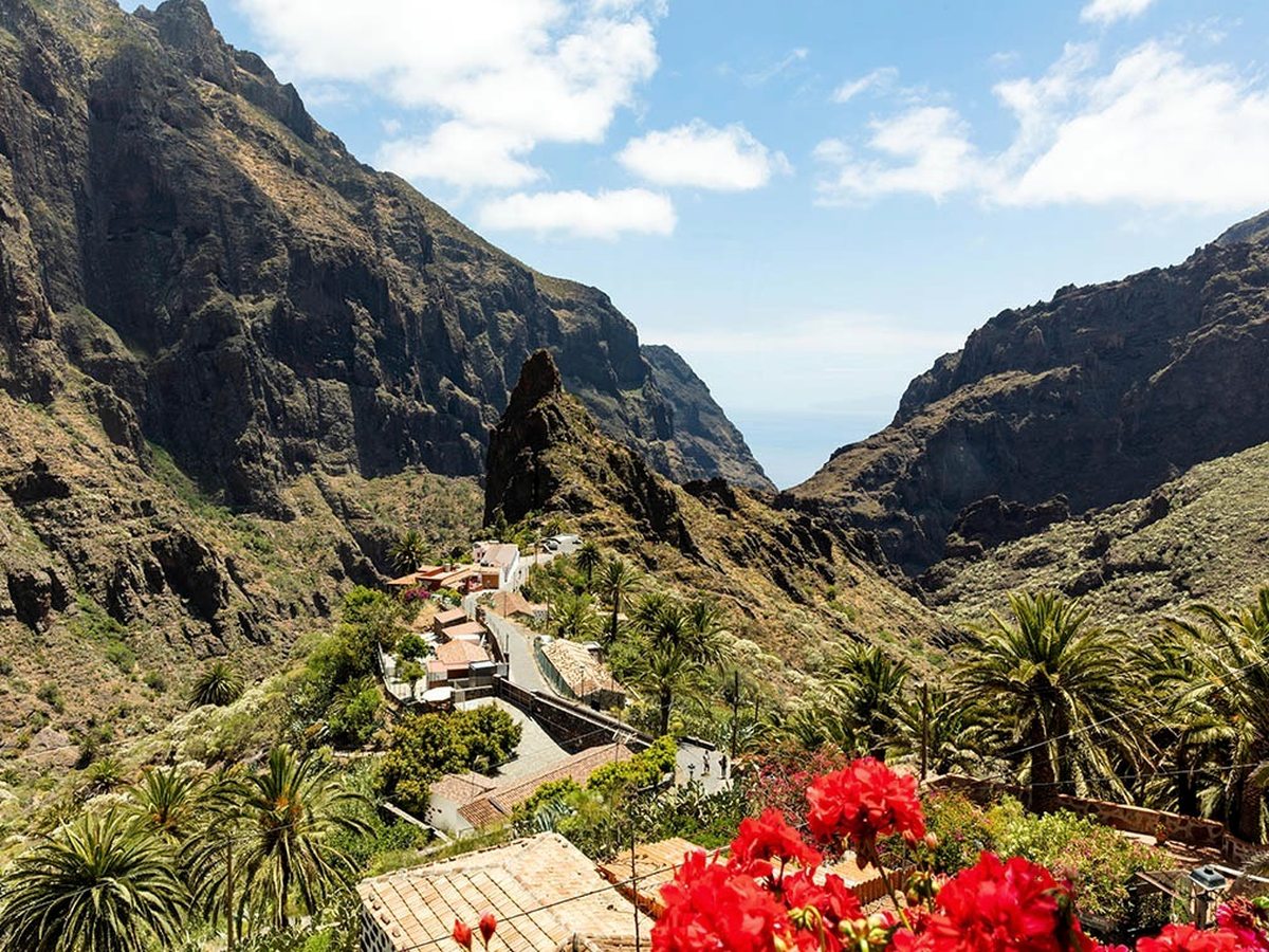 The terracotta rooftops of Masca village deep in a green mountain gorge, a rock pinnacle rising behind.