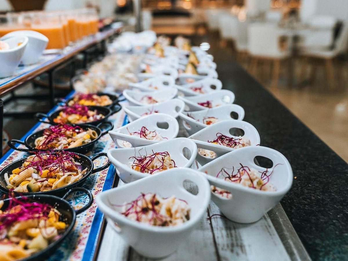 A row of white serving bowls of prepared salads along a dark buffet counter.