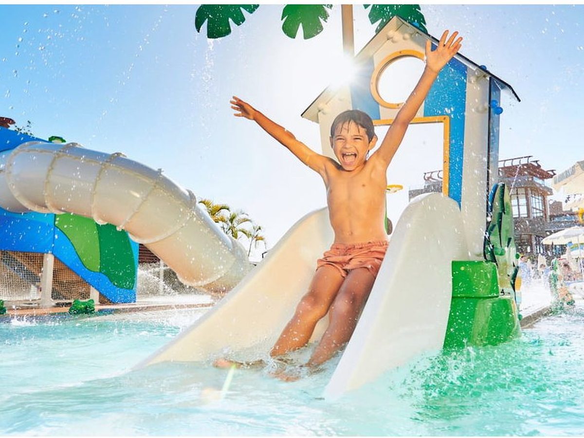 Child sliding down a small waterslide into the shallow water of a colourful children's splash park.