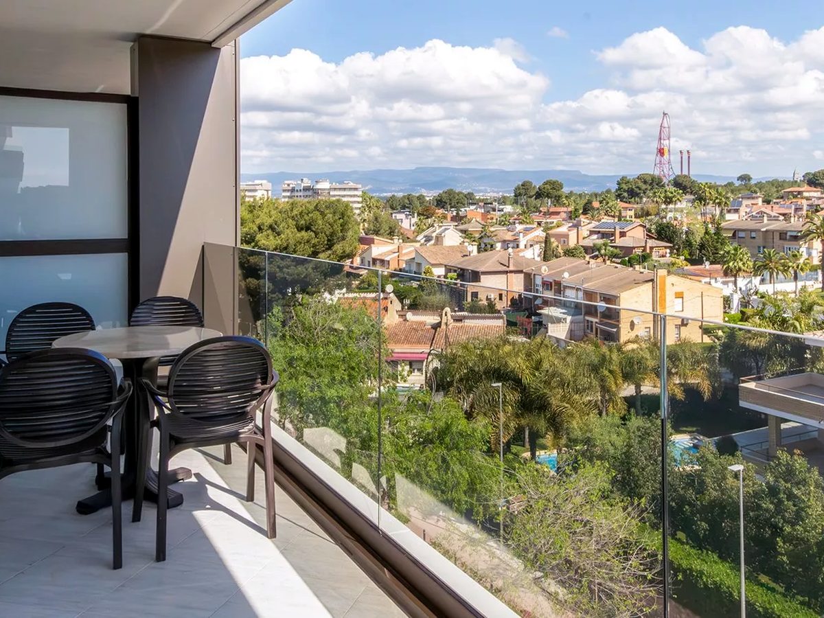 View from a suite balcony over the tiled rooftops and greenery of central Salou, with a PortAventura ride tower and hills on the horizon.