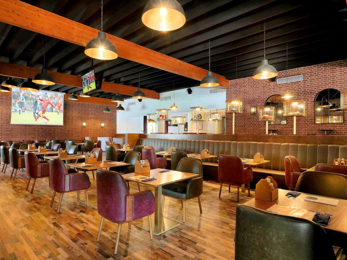 Indoor sports bar with flatscreen TVs on brick walls, timber beams, leather booths and dining tables under pendant lights.