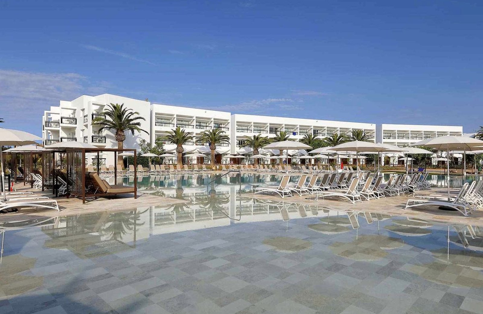 Grand Palladium Select Palace Ibiza: the main pool lined with loungers and parasols in front of the resort's long white low-rise building under a clear blue sky.