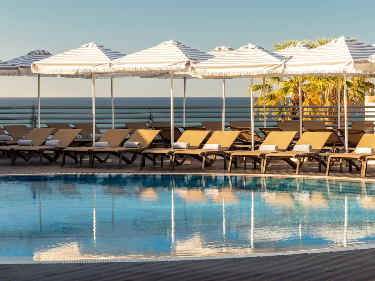 A curved pool edged with sun loungers and cream striped parasols, the sea on the horizon.