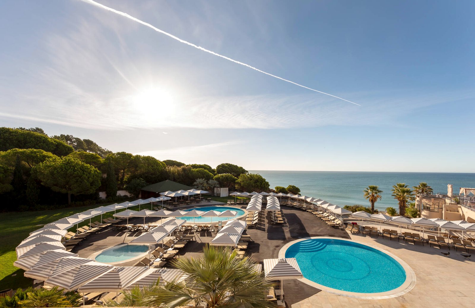 Grande Real Santa Eulália Resort & Hotel Spa: the resort's main pool terrace of round pools and striped parasols on the clifftop, with Santa Eulália beach and the sea beyond.