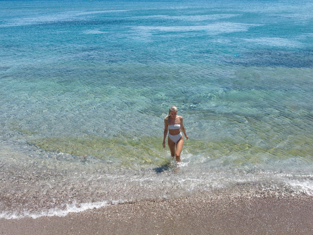 A woman wading into clear, shallow turquoise water off a gently shelving shore.