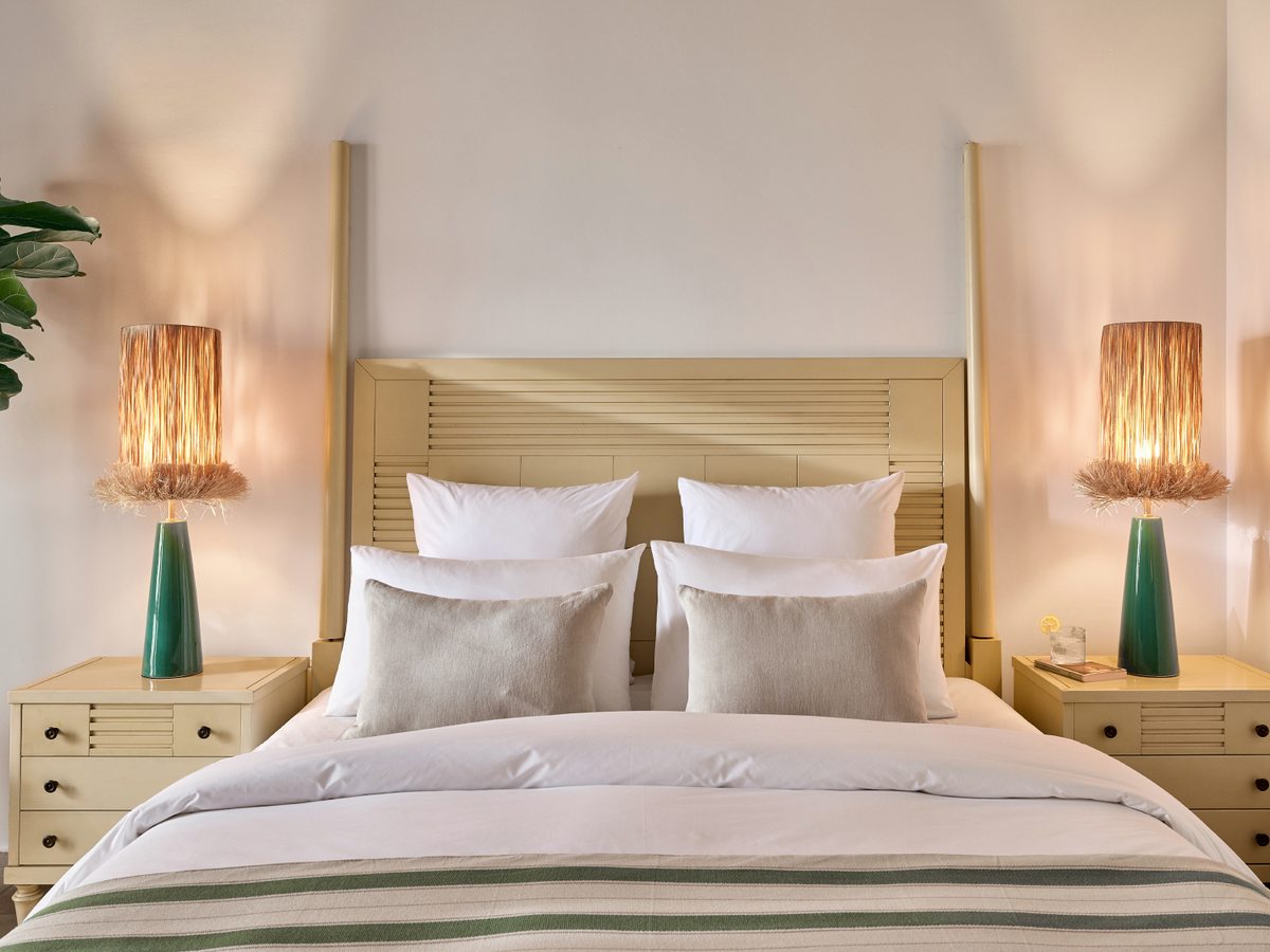 Double room with a king bed and pale woven headboard, wicker lamps on timber bedside tables and neutral decor.