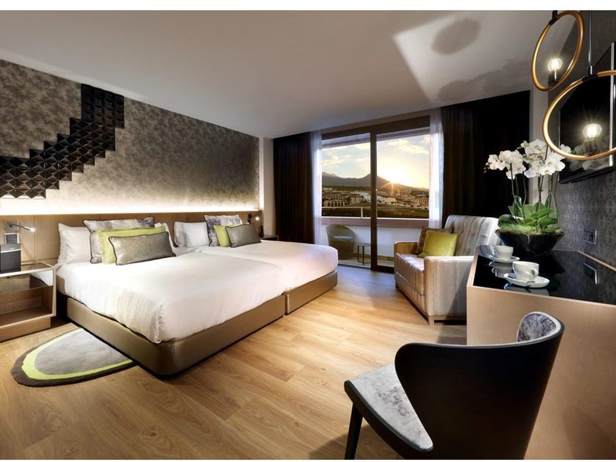 Bedroom with a king bed and a lounge chair, sliding doors onto a balcony with an inland mountain view.