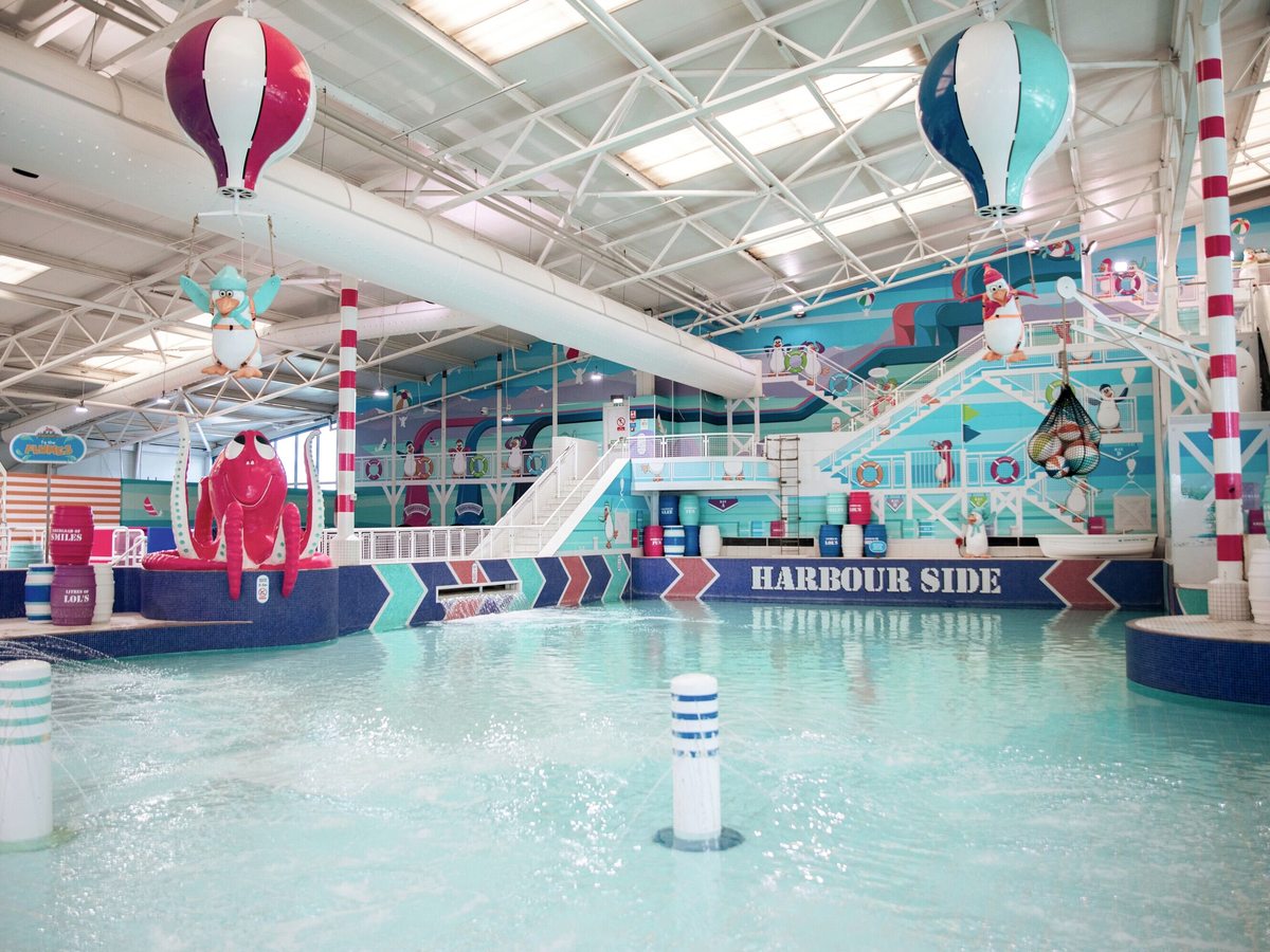 A shallow, zero-depth pool area with spray posts and a painted seaside mural, hot-air-balloon decorations hanging overhead.