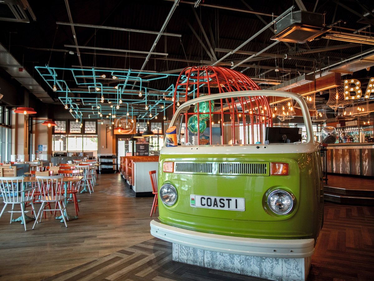 The interior of Coast House with a vintage green campervan converted into a service counter, communal tables and chairs and a bar beyond.