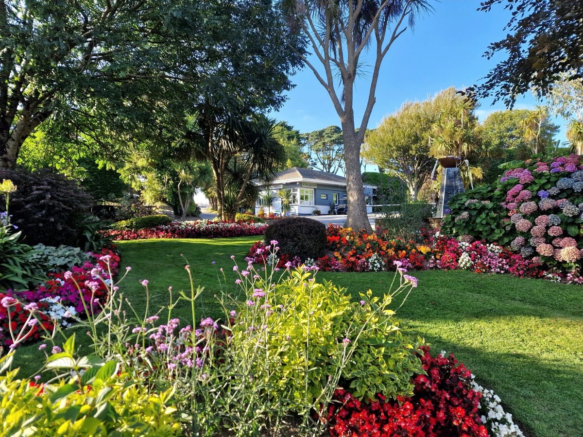 Colourful flower beds and mown lawns with holiday lodges among mature trees.