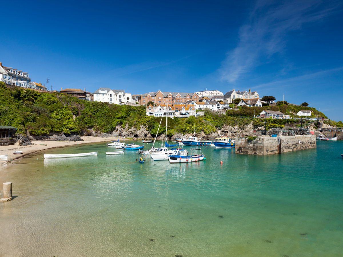 Newquay harbour with small boats, a sandy beach and the harbour wall below the town.